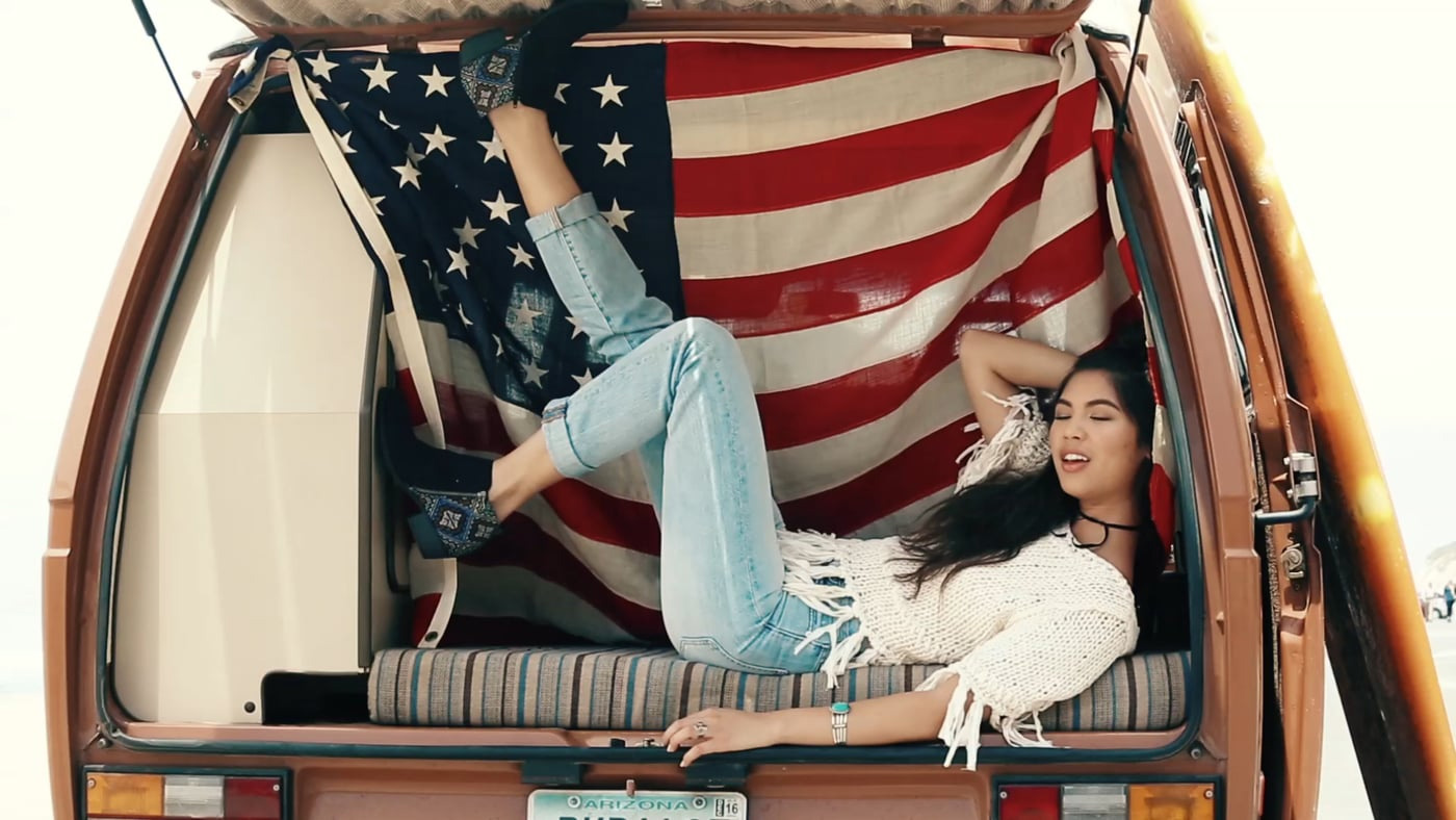 Girl lounging in back of van with American flag wearing Indigo Rd booties.